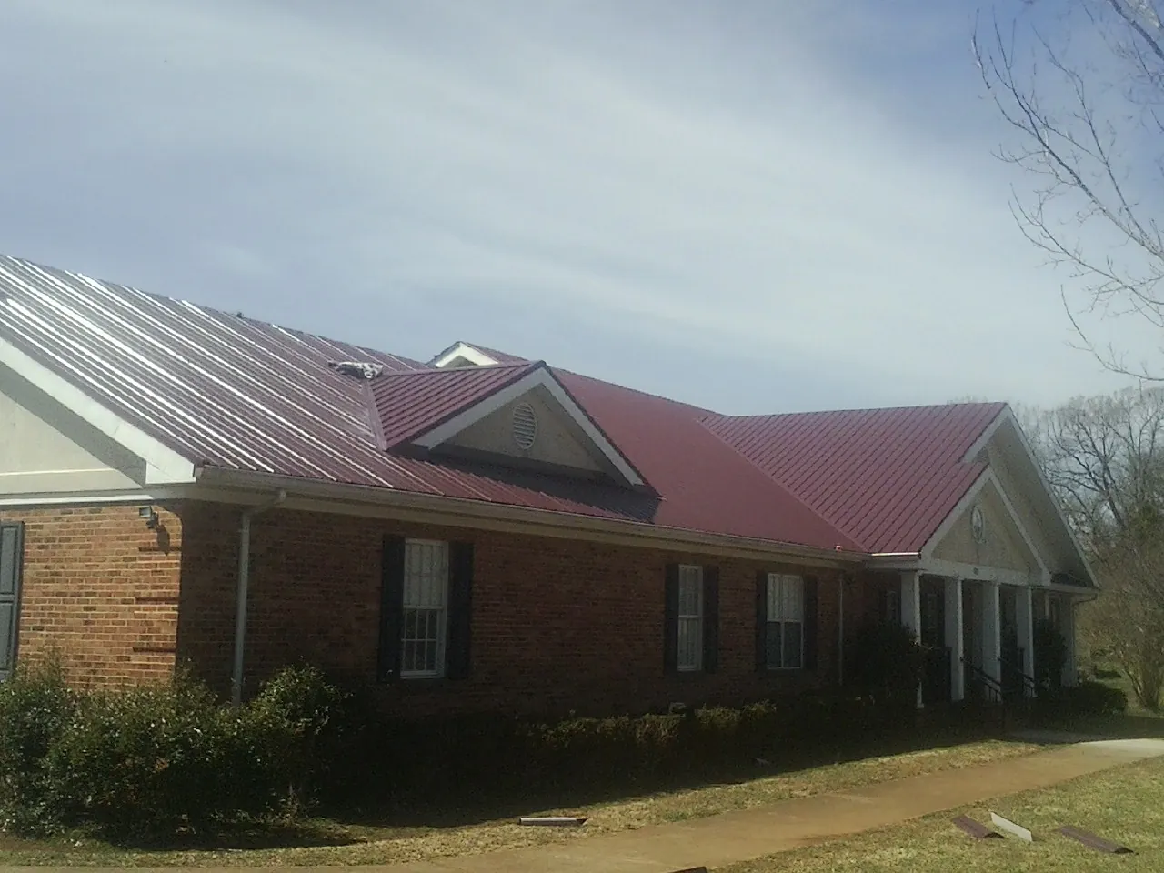 Red metal roof with gabled entries on a long brick building, from a Hail Damage Roof Repair job in Wenatchee