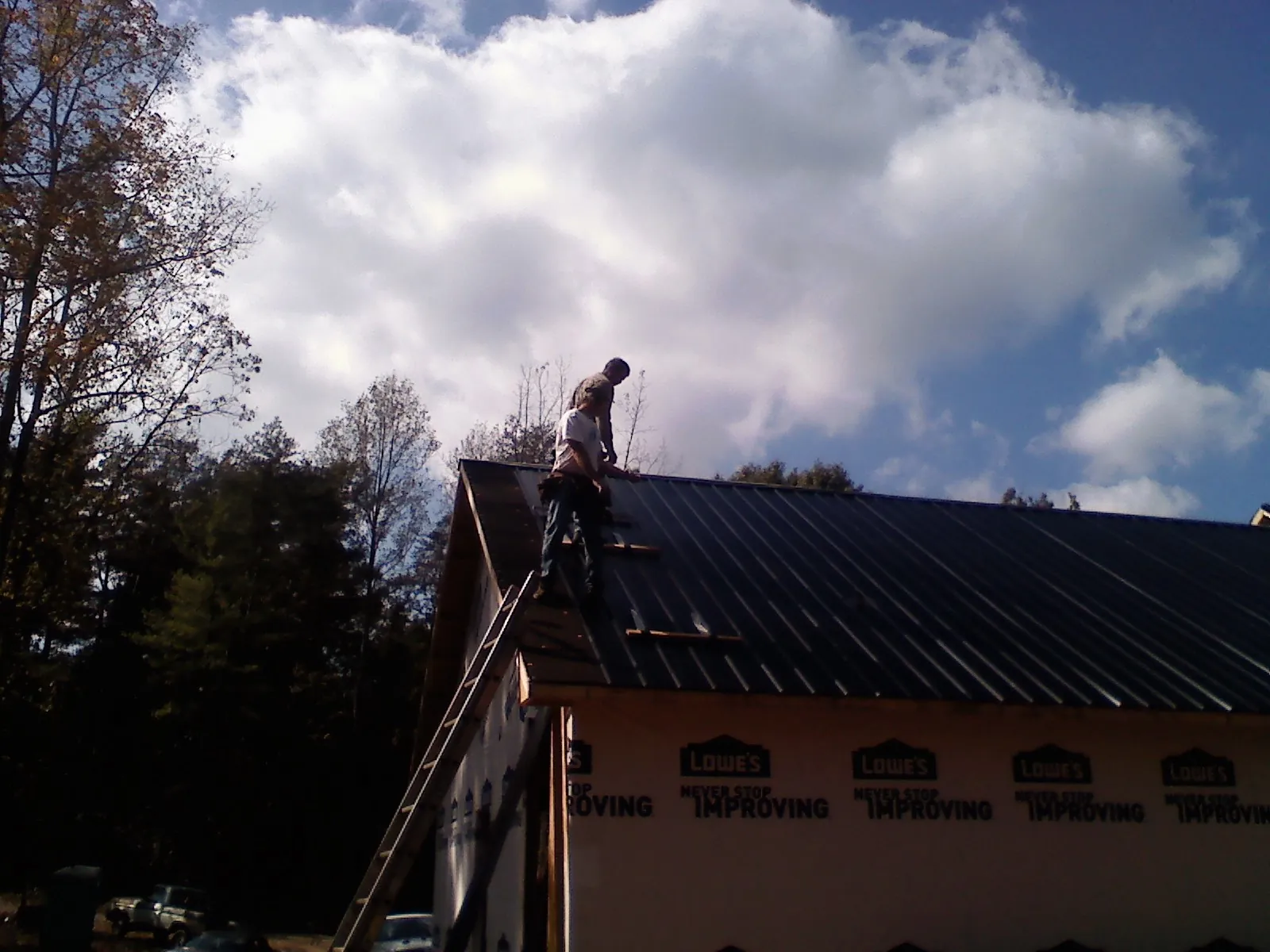Roofer fastening dark metal panels high against a cloudy sky, from a Roof Inspection job in Wenatchee