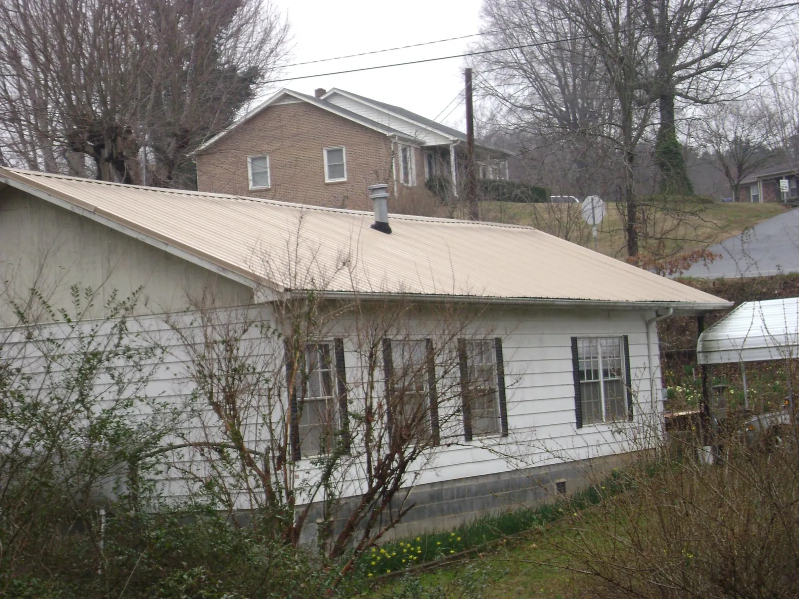 Tan metal roof on a white sided house set into a hillside — Commercial Roofing by Roofing Brothers in Wenatchee